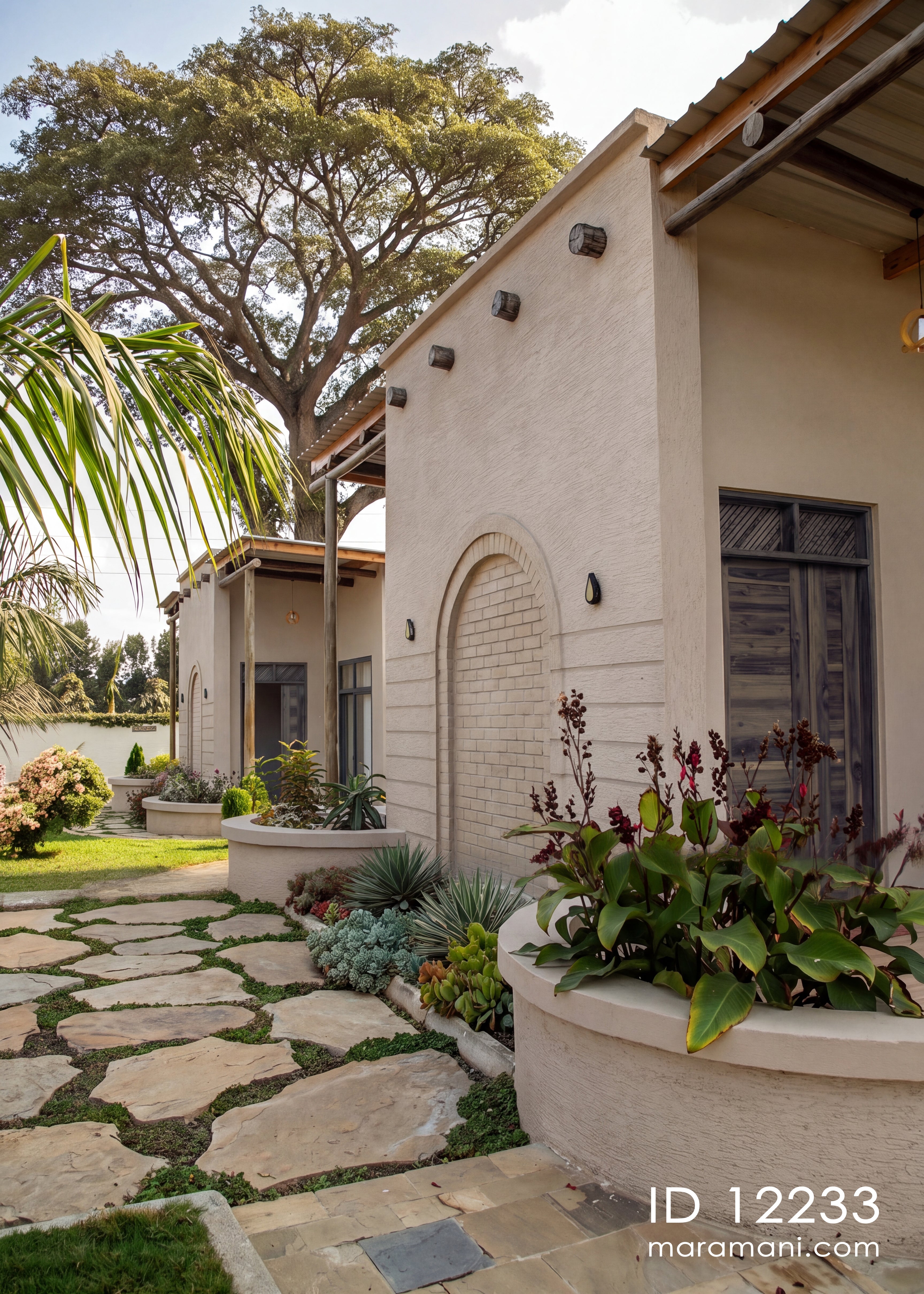 A Mediterranean-style villa exterior with beige stucco walls, a stone path, landscaped garden beds, and a large tree in the background.